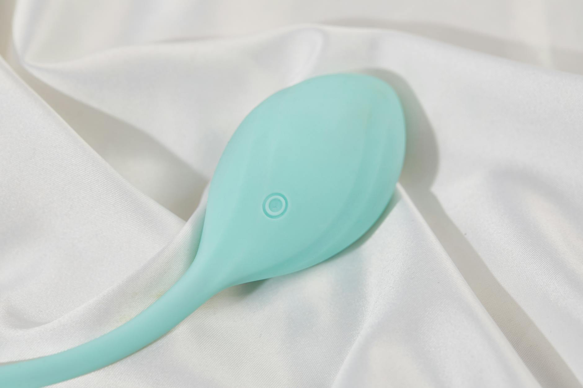 A sleek teal vibrator on smooth white silk, representing pleasure and arousal