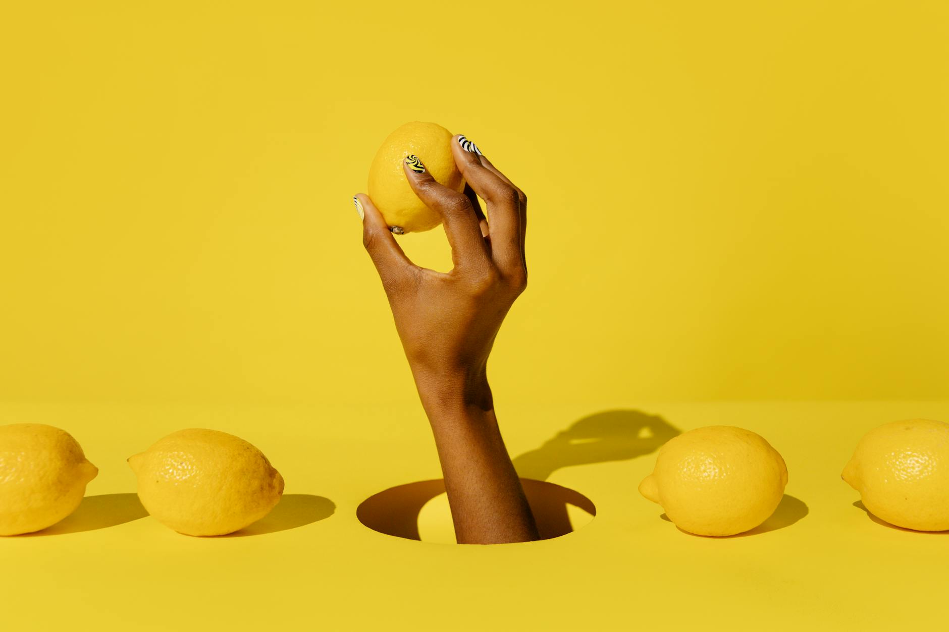 Hand holding a fresh lemon against a vivid yellow background, representing lemon clitoral vibrators