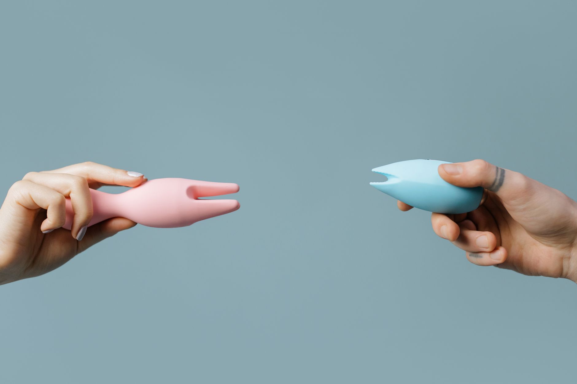 A hand holding two colorful silicone vibrators against a pastel background