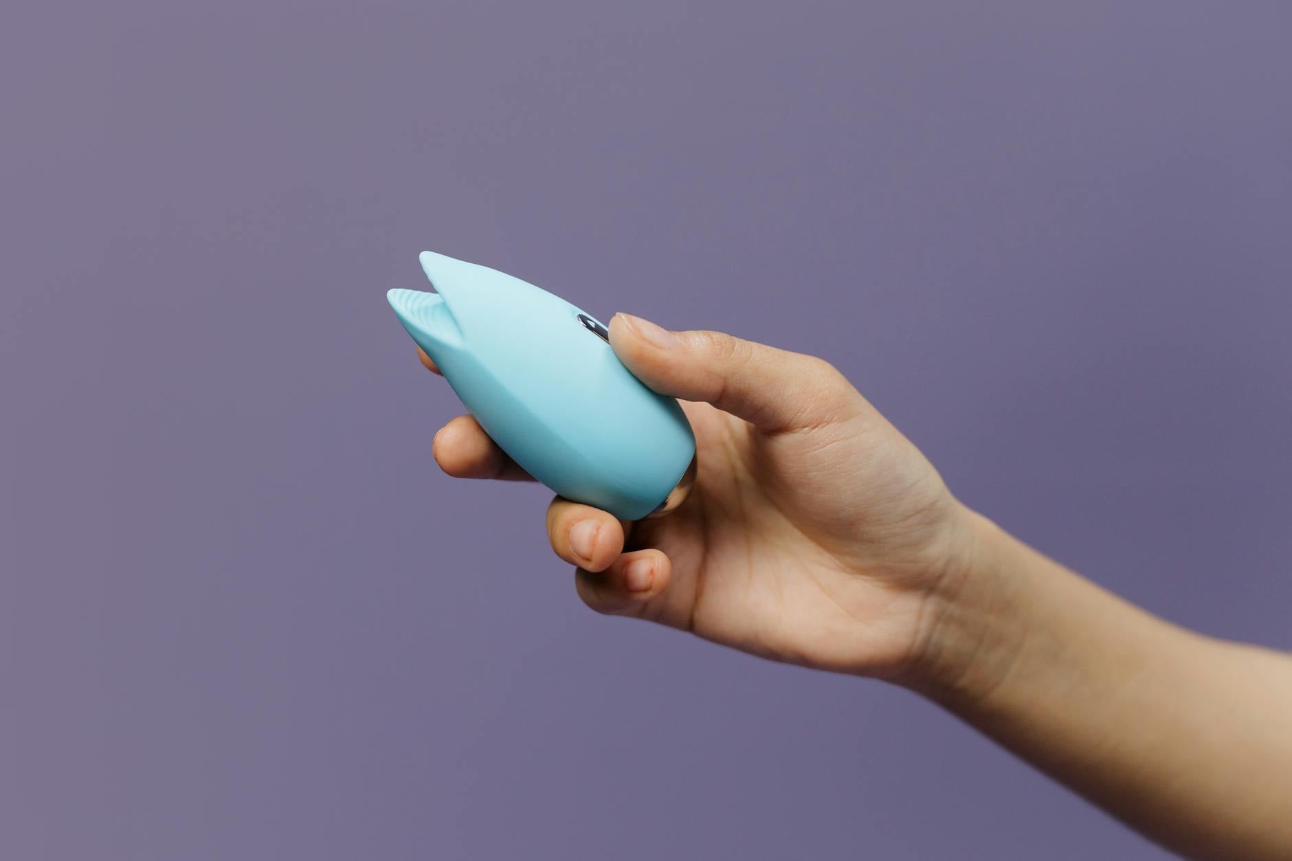 Woman with eyeglasses holding blue and pink silicone vibrators in a contemplative manner